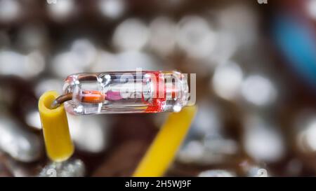 Nahaufnahme der alten Germanium-Punktkontaktdiode in versiegeltem Glasrohr. Retro-elektrisches Bauteil in transparentem Gehäuse mit zwei gelb isolierten Drähten. Stockfoto