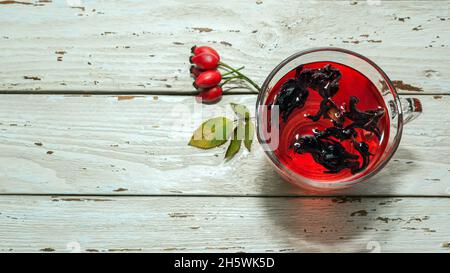 Natürlicher Tee aus wilden Rosenbeeren auf Holzbrettern. Homöopathie Behandlung von roten Beeren. Stockfoto