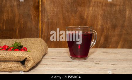 Natürlicher Tee aus wilden Rosenbeeren auf Holzbrettern. Homöopathie Behandlung von roten Beeren. Stockfoto