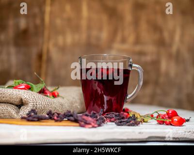 Natürlicher Tee aus wilden Rosenbeeren auf Holzbrettern. Homöopathie Behandlung von roten Beeren. Stockfoto