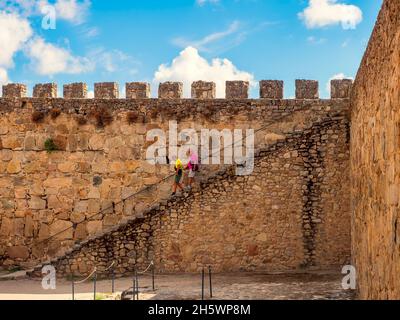 Zwei Personen, die an einem sonnigen Tag mit Wolken eine Treppe von der Fassade des Schlosses von Trujillo in Caceres herabsteigen. Stockfoto