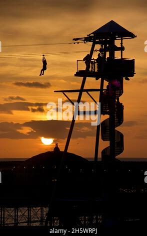 Reisen über die Seilrutscher-Attraktion, Brighton, England. Palace Pier und Sonnenuntergang Himmel dahinter. Stockfoto