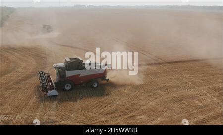 Im Hintergrund sammelt der Mähdrescher die Reste von Weizen. Neue Erntemaschinen auf dem Feld sammeln Weizen. Panoramablick auf das Feld von colle Stockfoto