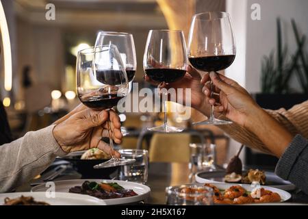 Nahaufnahme der Hände mit Gläsern beim Toasten von Rotwein im Restaurant - eine Gruppe von Freunden feiern klirrende Weingläser Stockfoto