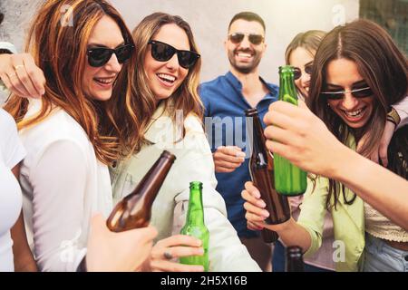 Fröhliche junge Leute, die Bierflaschen im Freien toasten - Millennials-Alkoholparty im Sommer - lebendige, farbgefilterte Bilder - konzentrieren sich auf das blo Stockfoto
