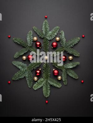 Weihnachtskarte mit einer dekorativen Schneeflocke aus Weihnachtsschmuck und Tannenzweigen auf schwarzem Hintergrund Stockfoto