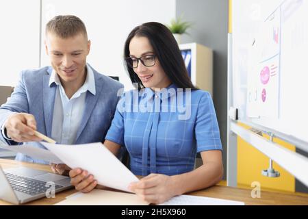 Geschäftsmann und -Frau sitzen am Tisch mit Dokumenten in den Händen und diskutieren Stockfoto