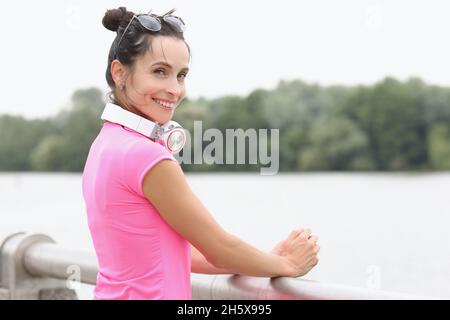 Junge lächelnde Frau mit Kopfhörern am Hals, die auf der Brücke steht Stockfoto