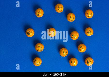 Jack o Laternen Kürbisse in Form von dekorativen Perlen oder Kugeln auf minimalistischem blauem Hintergrund mit Kopierraum verstreut. Süßigkeiten, Süßigkeiten, Trick-or-tr Stockfoto