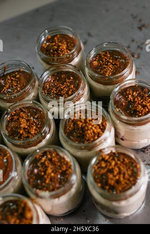 Von oben Glas Gläser mit köstlichen Schicht Dessert mit weißer Creme mit Karamell Topping und zerkleinerten Nüssen auf dem Tisch in der Küche dekoriert Stockfoto