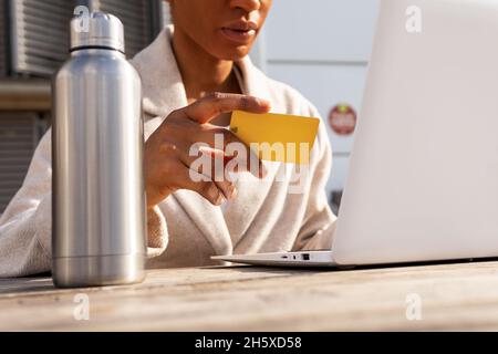 Crop anonyme weiblich mit Kreditkarte in der Hand tippen auf moderne Netbook, während Online-Kauf auf der Straße in der Stadt Stockfoto