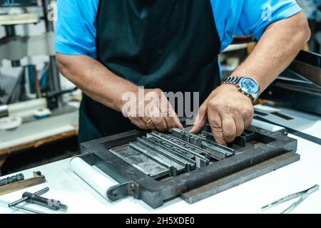 Hoher Erntewinkel unkenntlich älterer männlicher Handwerker in Schürze und Brille, der Metallrahmen für den Buchdruck im Studio vorbereitet Stockfoto