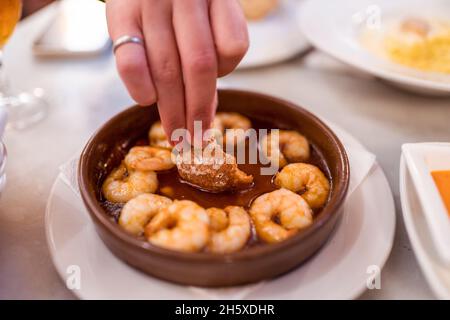 Von oben der Ernte unkenntlich Frau Dipping Brotscheibe in Sauce von appetitlich traditionellen Gambas al ajillo Gericht in Schüssel im Restaurant serviert Stockfoto