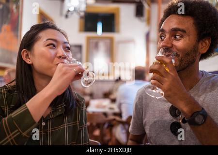 Der weiche Fokus des multirassischen Paares, das während einer festlichen Veranstaltung zusammen im modernen Restaurant zu Abend trinkt Stockfoto
