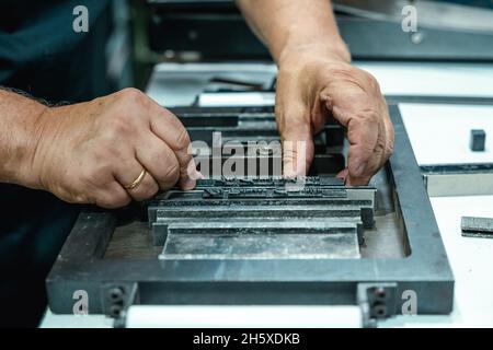 Hoher Erntewinkel unkenntlich älterer männlicher Handwerker in Schürze und Brille, der Metallrahmen für den Buchdruck im Studio vorbereitet Stockfoto