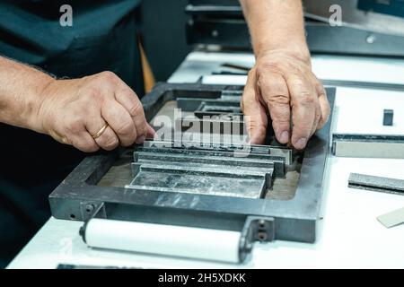 Hoher Erntewinkel unkenntlich älterer männlicher Handwerker in Schürze und Brille, der Metallrahmen für den Buchdruck im Studio vorbereitet Stockfoto
