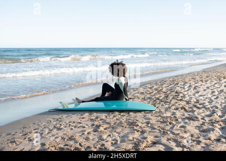 Rückansicht Ganzkörper einer anonymen Barfuß-Surferin im Neoprenanzug am Sandstrand in der Nähe des winkenden Meeres Stockfoto