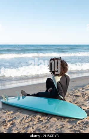 Rückansicht Ganzkörper einer anonymen Barfuß-Surferin im Neoprenanzug am Sandstrand in der Nähe des winkenden Meeres Stockfoto