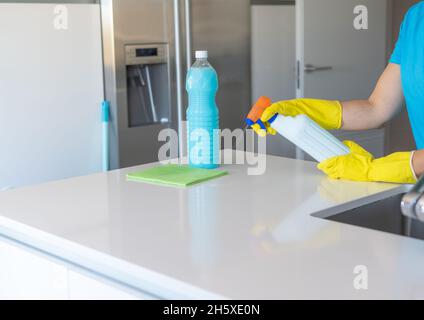 Crop anonyme Frau in gelben Gummihandschuhen sprühen Reinigungsmittel auf Tuch, während leichte Küche reinigen Stockfoto
