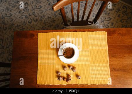 Draufsicht auf eine Tasse frisch gebrühten Espresso auf einer Untertasse, die auf Serviette in der Nähe von Eicheln auf einem Holztisch platziert wurde Stockfoto