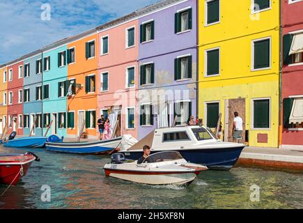 Junger Mann im Schnellboot vor bunten Häusern, Fondamenta di Cao Moleca, Burano, Venedig, Italien Stockfoto