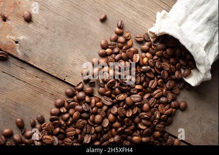 Kaffeebohnen fallen aus einem weißen Sack auf einem alten Holzhintergrund. Speicherplatz kopieren Stockfoto