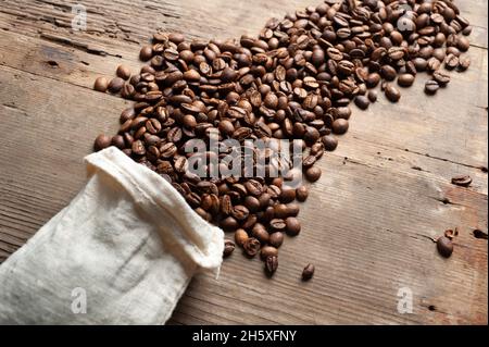 Kaffeebohnen fallen aus einem weißen Sack auf einem alten Holzhintergrund. Speicherplatz kopieren Stockfoto