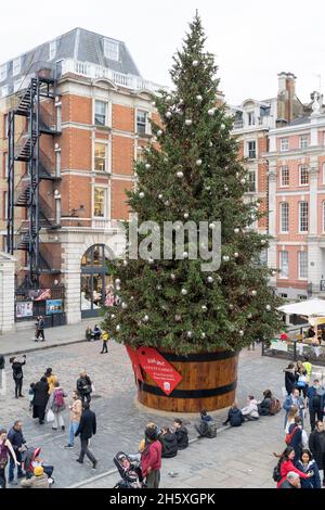 Am Covent Garden Square, einem riesigen Weihnachtsbaum, der mit Blasen und Bändern geschmückt ist, genießen Touristen die Festivalatmosphäre im West End London, England Stockfoto