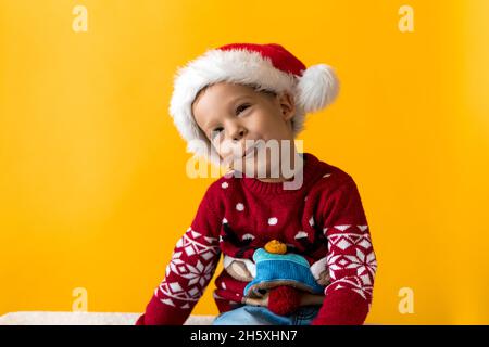 Porträt von glücklich lächelnd positive fröhlich positive Vorschule kleinen Jungen in rot warmen weihnachtsmann Hut zeigt Daumen nach oben auf orange, gelben Hintergrund. Winter Stockfoto