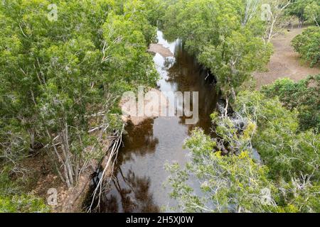 Flaches Wasser in einem von Bäumen gesäumten ländlichen Bach mit Baumreflexen - Drohnenlandschaft Stockfoto
