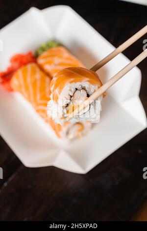 Philadelphia-Rolle mit Chopstics für Sushi halten. Rollen Sie mit Lachs, Garnelen und Mango. Lieferung japanischer Speisen Stockfoto