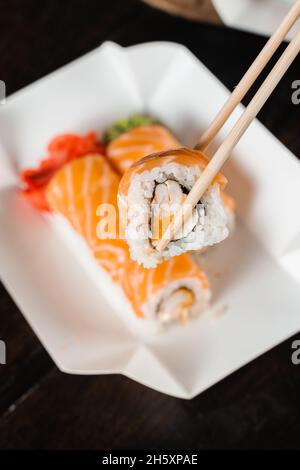 Philadelphia-Rolle mit Chopstics für Sushi halten. Rollen Sie mit Lachs, Garnelen und Mango. Lieferung japanischer Speisen Stockfoto