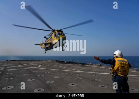 GOLF VON OMAN (NOV 11, 2021) Thomas schnell, der Mate 2. Klasse des Bootswains, signalisiert einem pakistanischen Seekönig, als er während einer Passing-Übung im Golf von Oman am 11. November vom Flugdeck des amphibischen Dock-Landungsschiffes USS Pearl Harbor (LSD 52) abhebt. Pearl Harbor und die 11. Marine Expeditionary Unit werden im Einsatzgebiet der 5. US-Flotte eingesetzt, um Marineinteroperationen zu unterstützen, um die maritime Stabilität und Sicherheit in der Zentralregion zu gewährleisten und das Mittelmeer und den Pazifik durch den westlichen Indischen Ozean und drei strategische Engpässe zu verbinden. (USA Navy Foto von Mass Commu Stockfoto