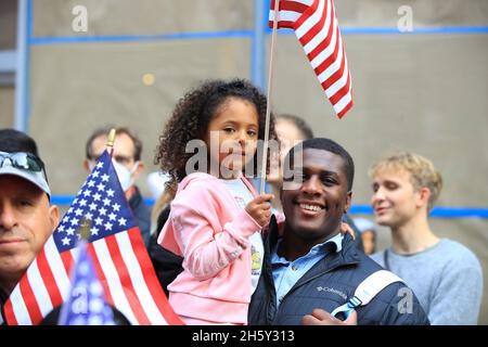 New York, N.Y/USA – 11. November 2021: Ein Kind, das von Vater gehalten wird, schwingt während der Veterans Day Parade auf der Fifth Avenue in New York am 11. November 2021 eine Flagge der Vereinigten Staaten. Quelle: Gordon Donovan/Alamy Live News) Stockfoto