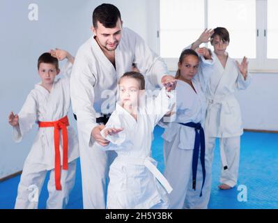 Kleine Kinder machen Karate-Kicks mit männlichem Trainer Stockfoto