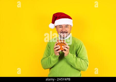 hispanischer älterer Mann mit einem Tonkrug Kaffee oder Fruchtpunsch zu weihnachten auf gelbem Hintergrund in lateinamerika Stockfoto