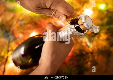 Eröffnungsflasche Sekt wie Champagner, eine Menschenhand, Neujahrslichter, glückliches neues Jahr und Weihnachten, Feier Stockfoto