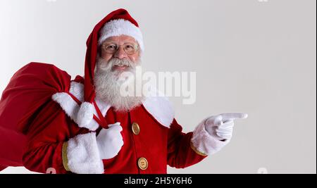 Foto des Weihnachtsmannes mit Handschuhen in Zeigegeste. Der Weihnachtsmann zeigt mit den Fingern auf Weiß. Stockfoto
