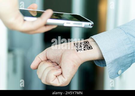 Hand mit qr-Code am Handgelenk. Zukunft der politischen Bevölkerungskontrolle. Chippisierung der Menschen. Scannen Sie den QR-Code mithilfe der mobilen Anwendung. Nachweis der Complet Stockfoto