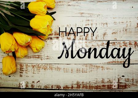 Happy Monday Text und Bouquet von gelben Tulpen auf weißem Holzhintergrund Stockfoto