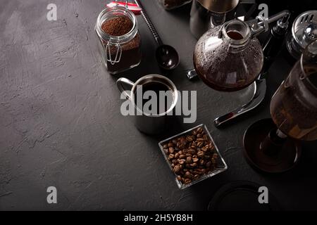 Vakuum-Kaffeemaschine auch als vac-Topf, Siphon oder Syphon Kaffeemaschine bekannt. Metallbecher und geröstete Kaffeebohnen auf rustikalem Tisch aus schwarzem Stein. Kopieren Sie den SPAC Stockfoto