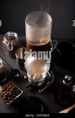 Vakuum-Kaffeemaschine auch bekannt als vac-Topf, Siphon oder Syphon Kaffeemaschine und geröstete Kaffeebohnen auf rustikalen schwarzen Stein Tisch. Stockfoto