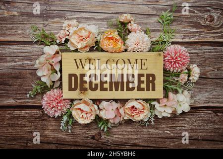 Willkommen Dezember Text auf Holzbrett mit Blumen Rahmen auf Holz Hintergrund Stockfoto