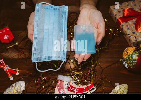 Weihnachtsgeschenk - Gesichtsmaske und antiseptisch. Pov oben Nahaufnahme über der Ansicht von oben Foto von weiblichen Händen mit weihnachtsgeschenk auf Tischhintergrund Stockfoto