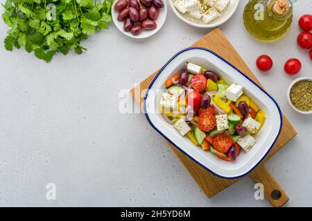 Gekochter griechischer Horiatiki-Salat aus dem Dorf. Köstliche und frische Zutaten. Teller mit Lebensmitteln auf Schneidebrett. Oliven, Oli in der Flasche, Kirschtomaten, Gewürz, Stockfoto