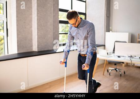 Arbeiter Mit Krücken Am Arbeitsplatz Oder Im Büro. Rehabilitationsleistungen Stockfoto
