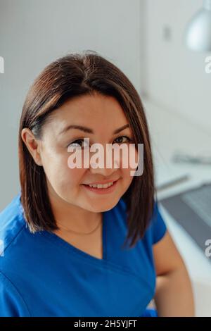 Porträt einer glücklichen Ärztin, die mit einem Laptop in Uniform an einem Tisch sitzt und die Kamera anlächelt Stockfoto