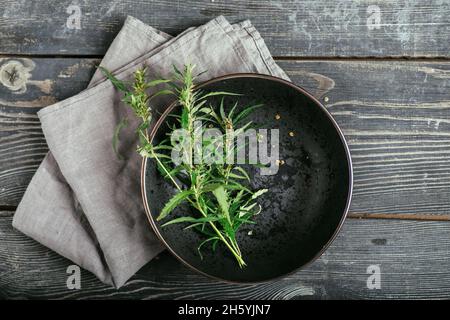 Cannabiszweig und Blätter auf einem schwarzen Teller und Holzhintergrund. Laborproduktion von Kosmetika mit CBD-Öl. Draufsicht Stockfoto