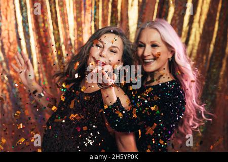 Zwei ältere Freundinnen mit Spaß im Studio blasen Konfetti Stockfoto