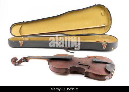 Breites Nahaufnahme-Studio-Aufnahme einer alten, gebrochenen, staubbedeckten Geige mit ihrem alten, zerkratzten Gehäuse, isoliert auf weißem Hintergrund. Vintage beschädigtes Musical Stockfoto